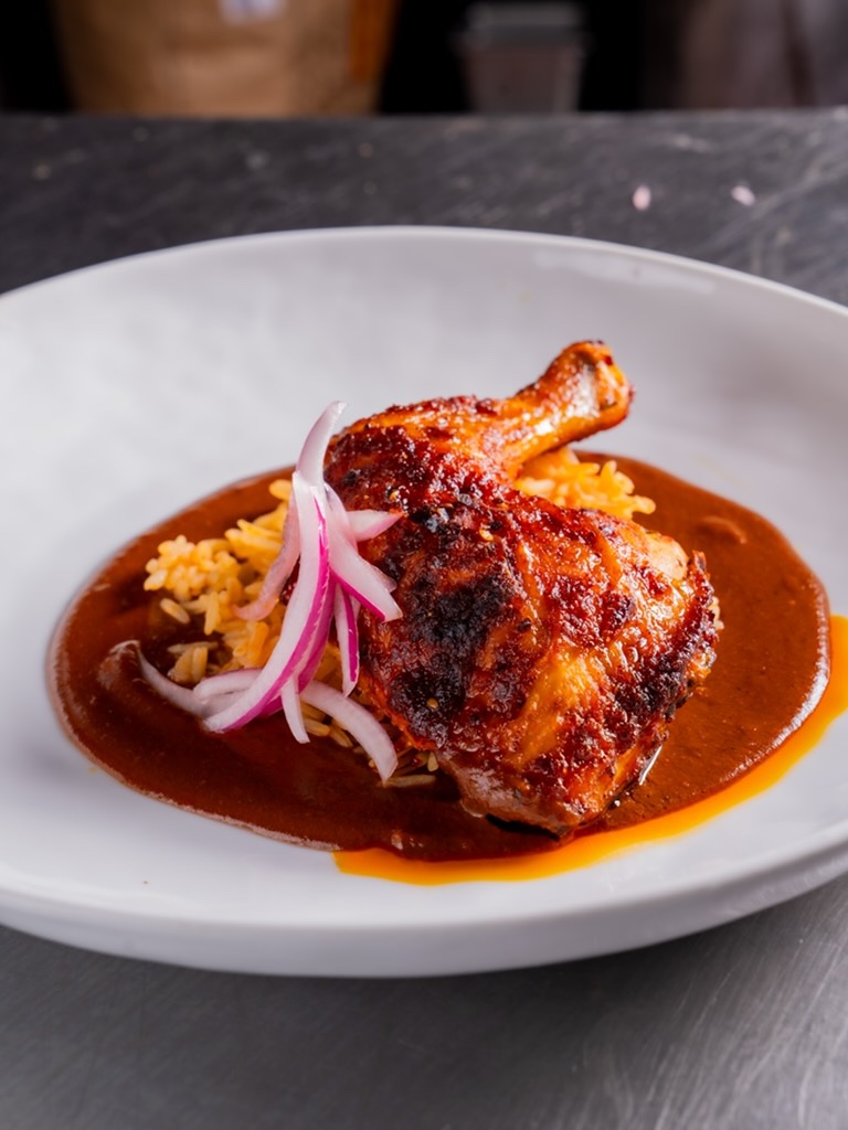 Roasted chicken leg over Mexican rice in red mole sauce with pickled red onion