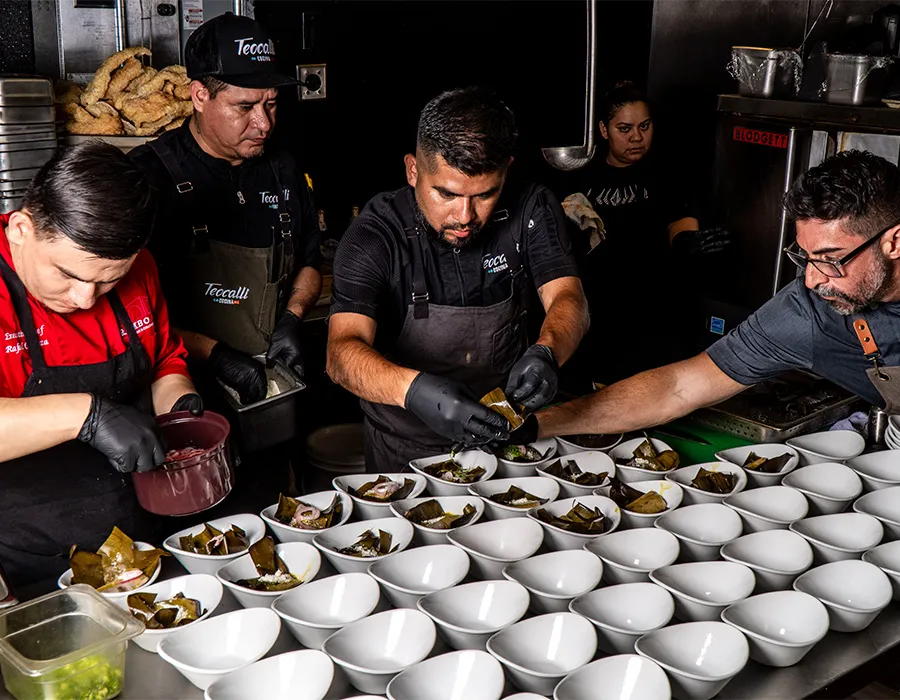 Chefs plating dozens of bowls on the line for an event