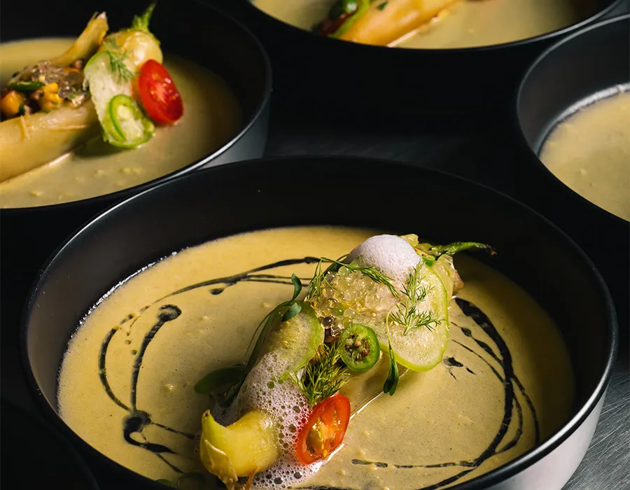 Creamy green soup garnished with chile slices, tomato, foam and herbs