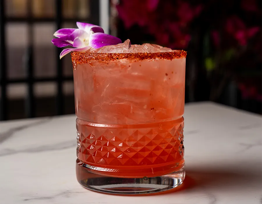 Red cocktail on the rocks with a chile-salt rim and an orchid garnish