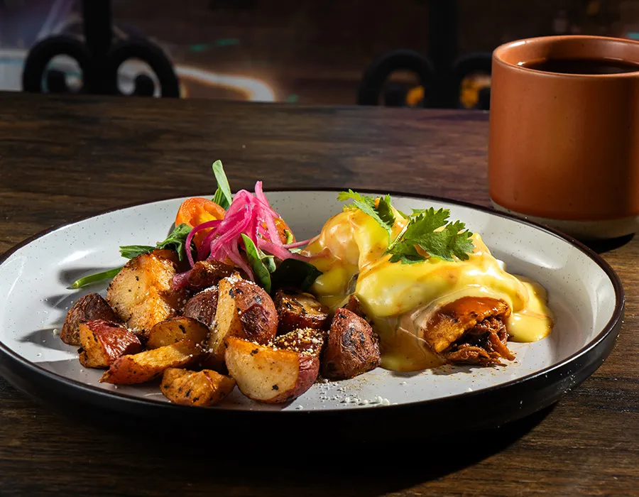 Brunch plate of breakfast potatoes and enchiladas with hollandaise, pickled onions and cilantro