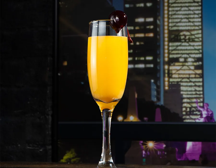 Mimosa in a champagne flute garnished with a cherry